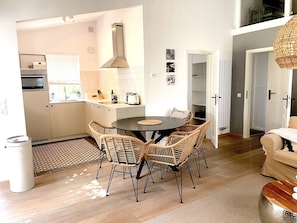 A modern kitchen with a dining area, featuring a round table, wicker chairs, and a built-in oven.