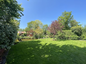 A well-maintained lawn with a variety of trees and shrubs, a small pond, and a house in the background.