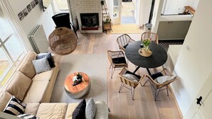 A modern living room with a sofa, round coffee table, wicker chairs, a fireplace, and a dining area with a round table.