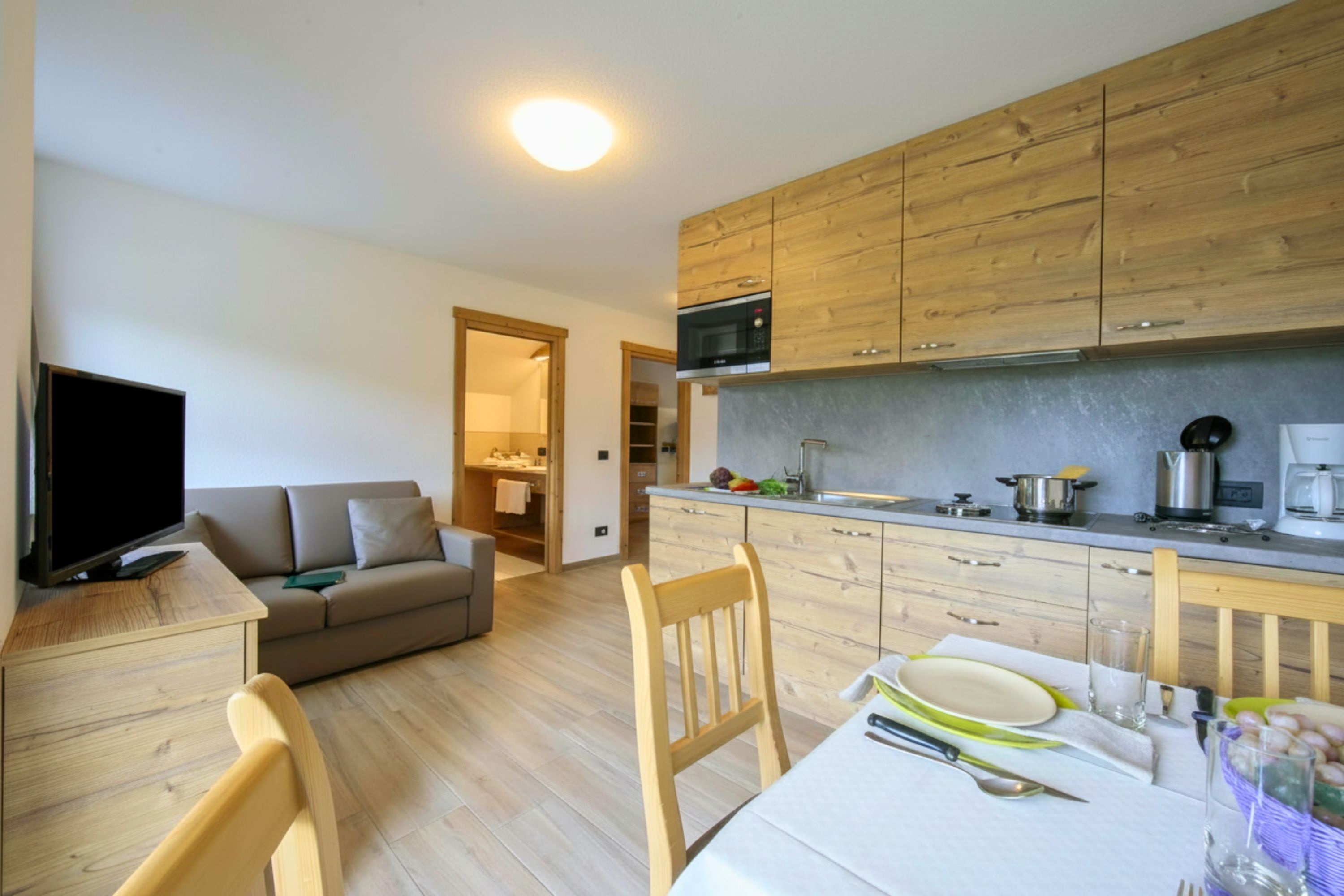 Una cocina moderna con armarios de madera, una mesa de comedor con sillas, un televisor y un sofá en la sala.