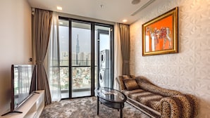 A modern living room with a glass door leading to a balcony, a leopard print sofa, a glass coffee table, and a mounted painting. - NES House - Riverview Apartment (Ho Chi Minh City)