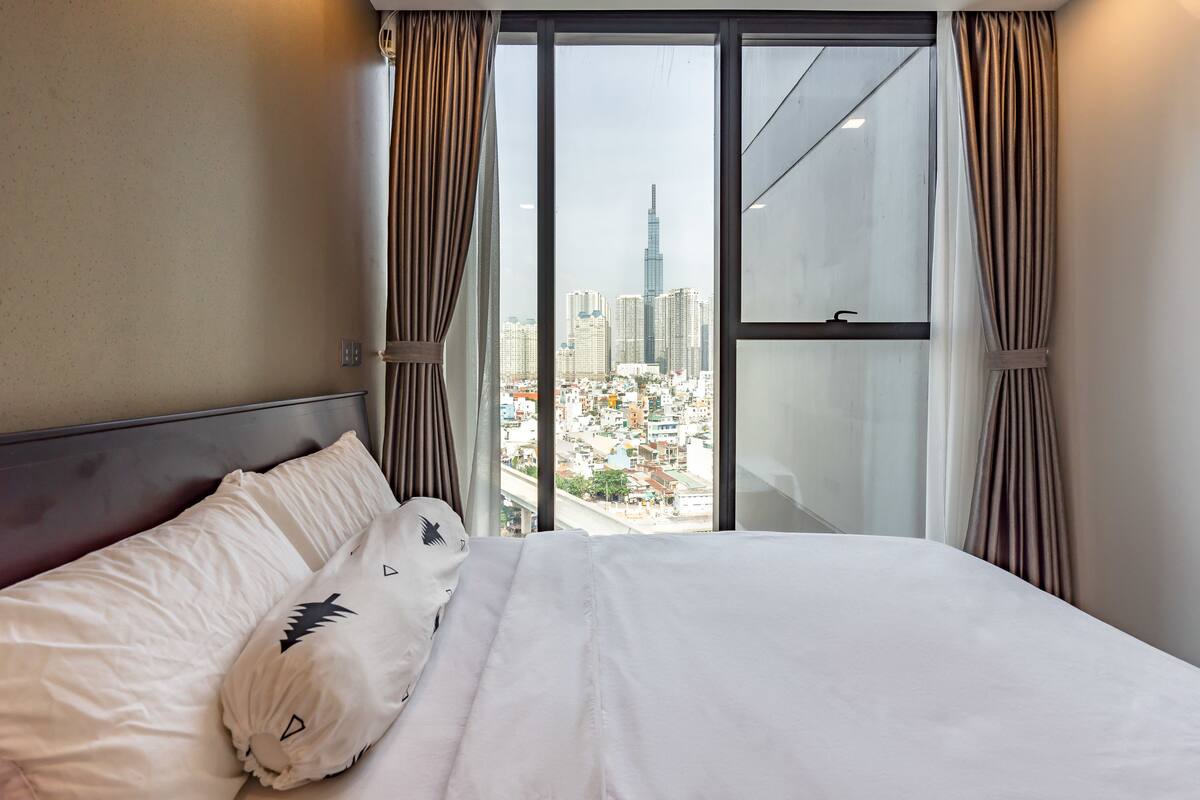 A hotel room with a large window offering a city view, a neatly made bed, and curtains.