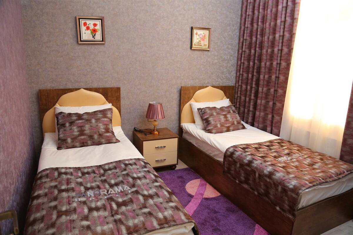 Een hotelkamer met twee bedden, een nachtkastje, een lamp en twee ingelijste foto’s aan de muur.