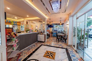 A restaurant interior with a tiled floor, a counter with snacks, a television, and a seating area. - Front One Budget Hotel Slamet Riyadi Solo (Surakarta)