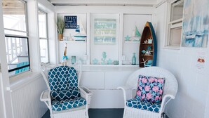 A cozy seating area with two wicker chairs, one with a blue geometric cushion and the other with a floral cushion, positioned in front of a window with a view of the outdoors.