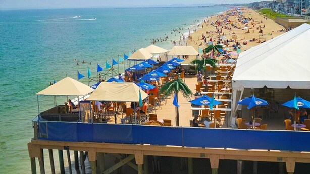 A beachside pier with outdoor seating and umbrellas, overlooking a crowded beach.