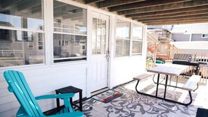 A covered patio with a turquoise chair, a small table, and a grill area.