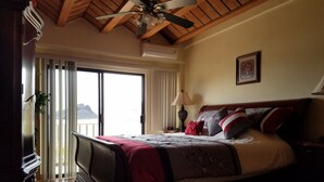 Een slaapkamer met een bed, een plafondventilator, een raam met uitzicht en een deur.