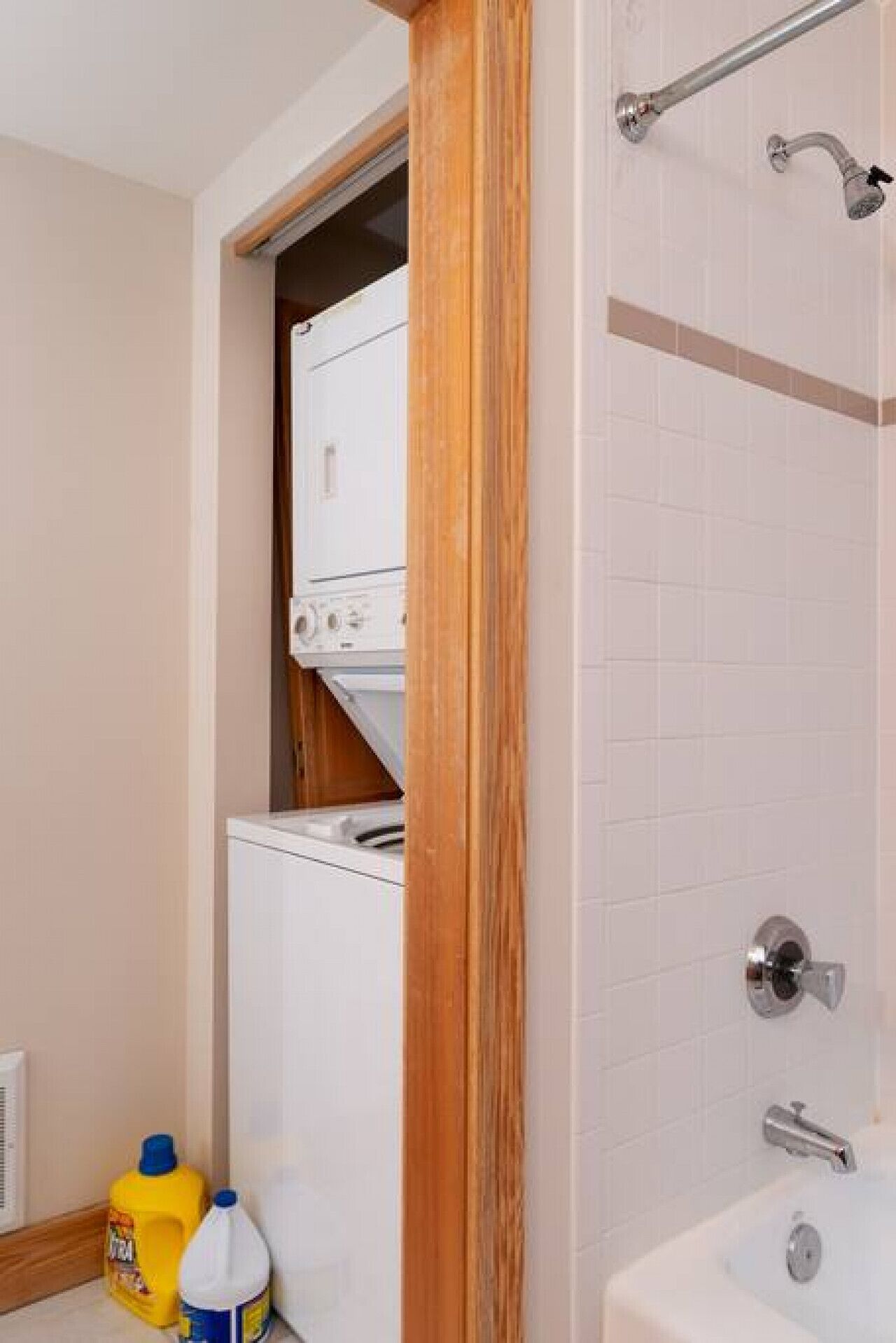 Un bagno con doccia, un water e un lavandino. Si nota una cornice di legno e una parete rivestita di piastrelle bianche.