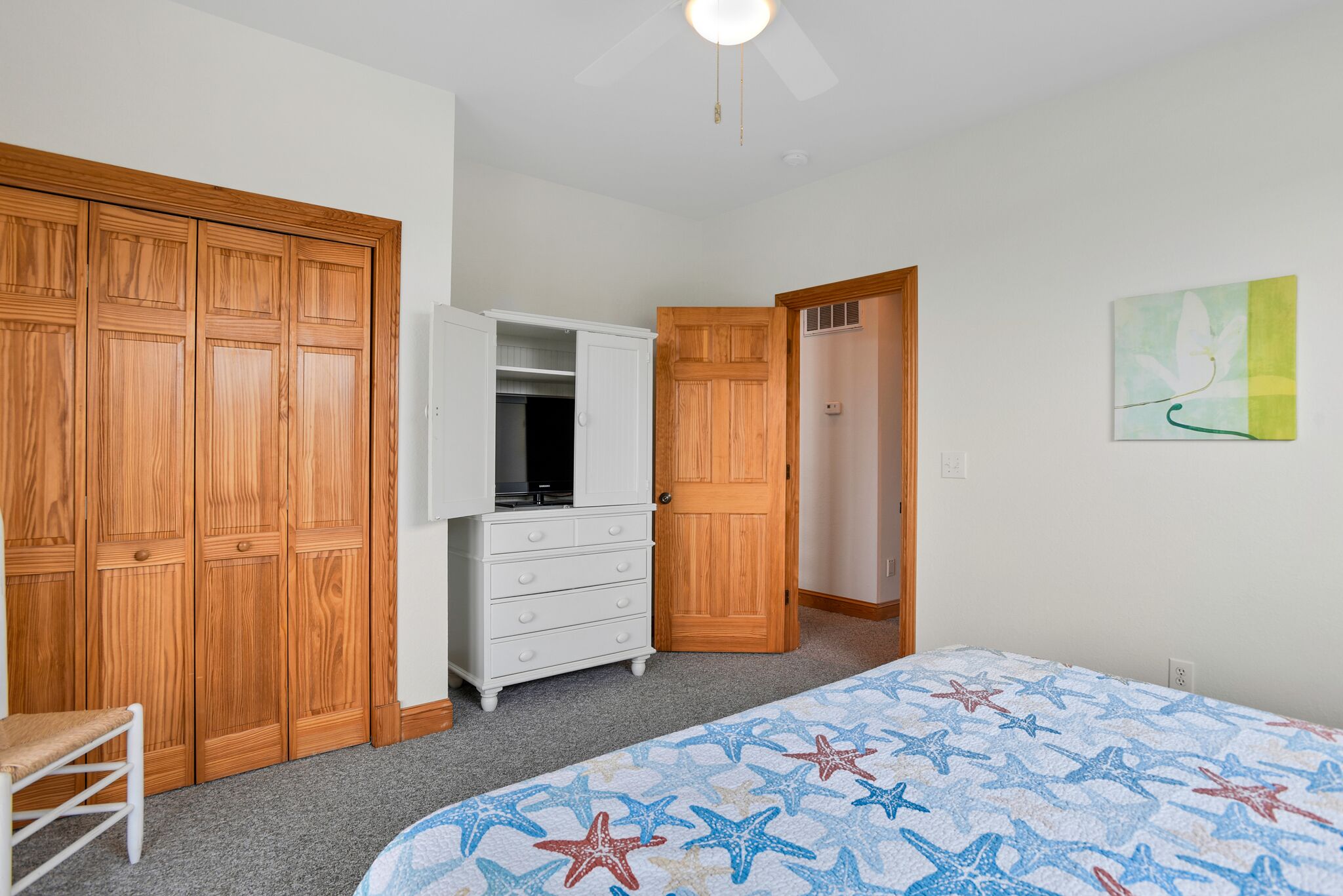 A bedroom with a bed, wooden wardrobe, white dresser, and a closet.