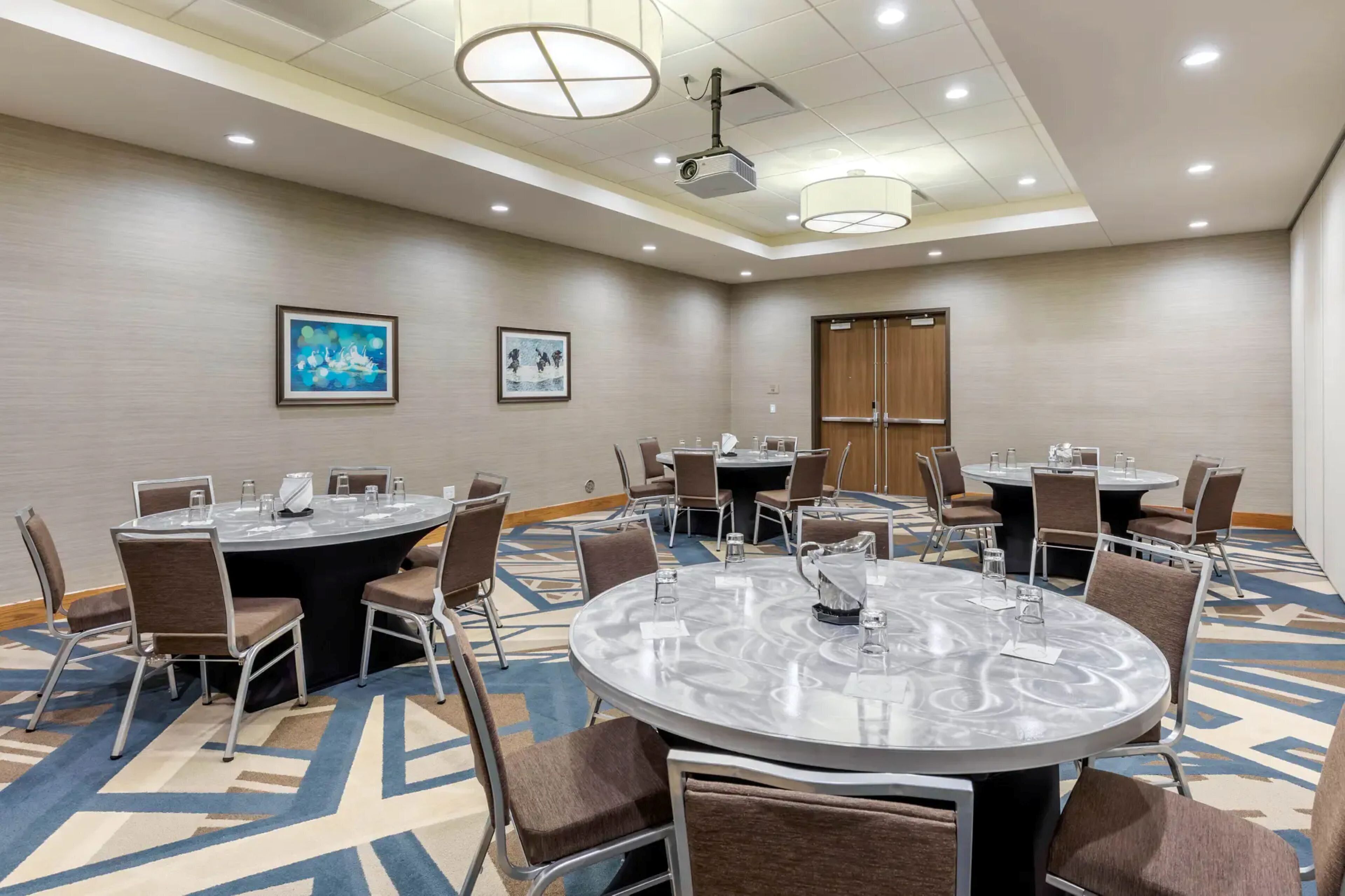 A conference room with round tables, chairs, a projector, and framed artwork on the walls.