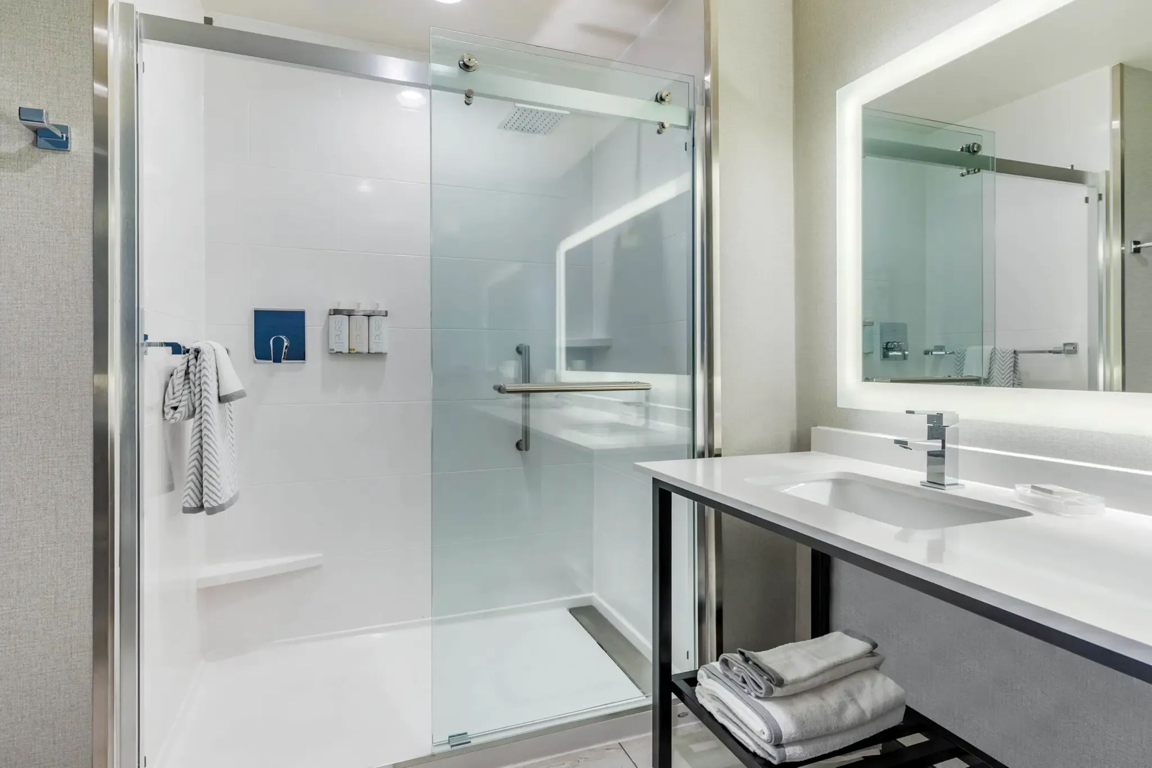 A modern bathroom with a glass-enclosed shower, a large mirror, and a white sink.