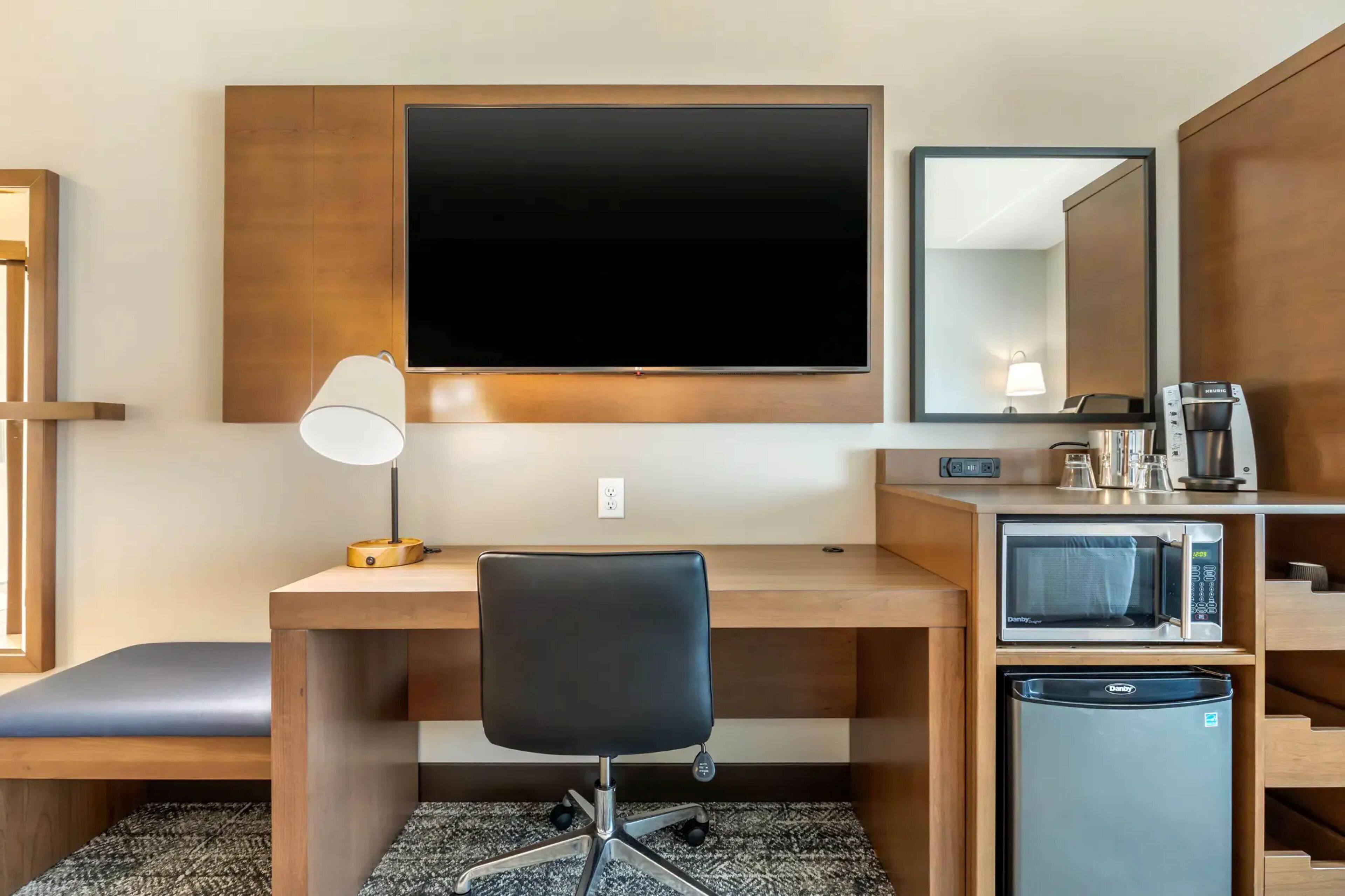 Une chambre d’hôtel équipée d’un bureau, d’une chaise, d’une télévision, d’un four à micro-ondes, d’un mini-réfrigérateur et d’une machine à café.
