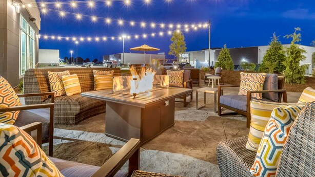 Una terrazza esterna con mobili in vimini, un elemento decorativo con fuoco e luci a tendina.