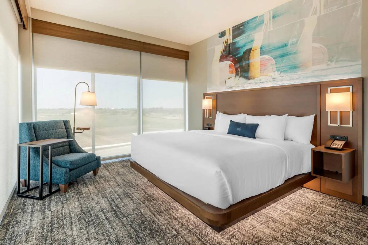 A hotel room with a large bed, a chair, a desk, and a painting on the wall.