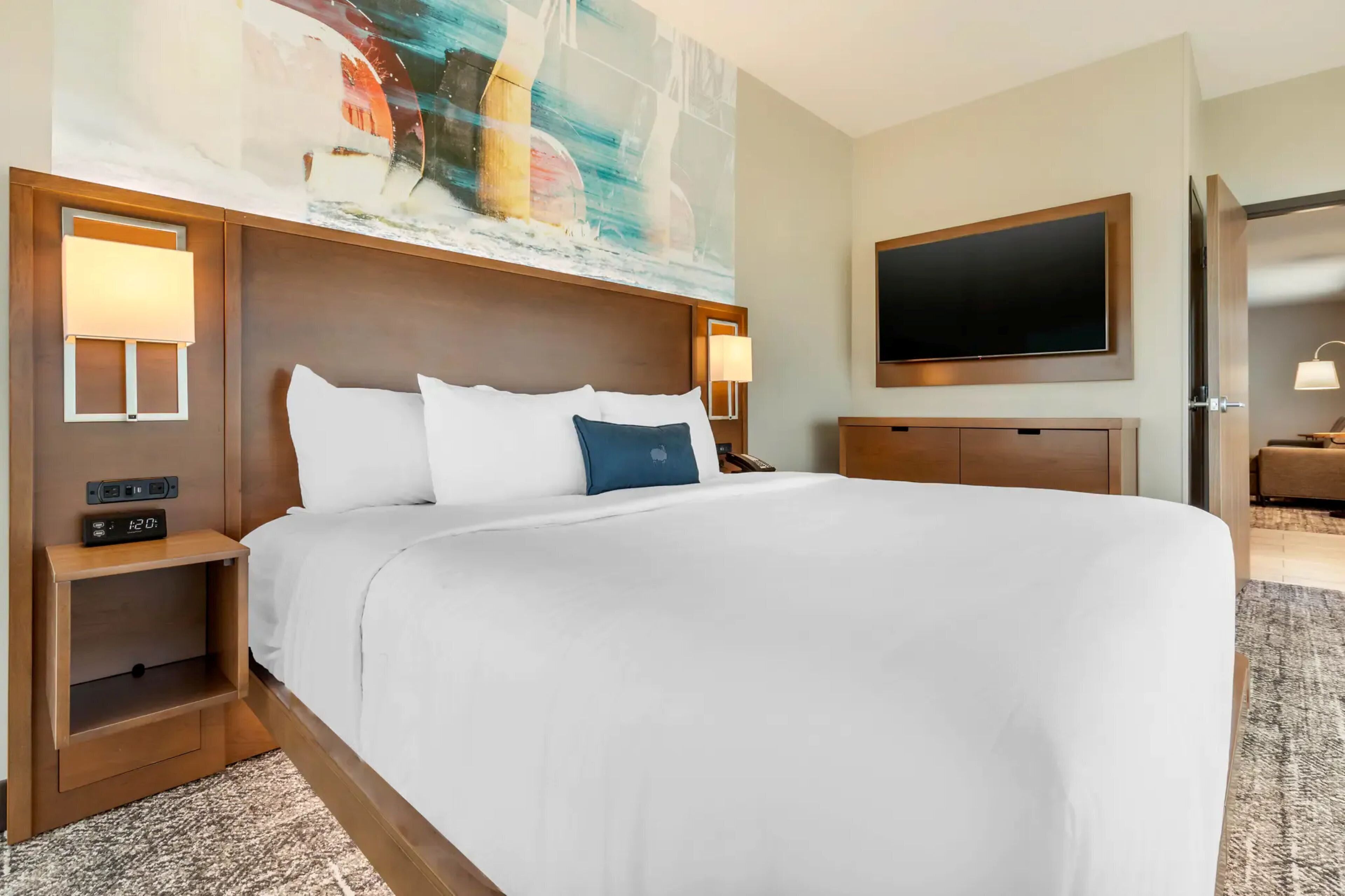 A hotel room with a large bed, bedside lamps, a flat-screen TV, and a painting on the wall.