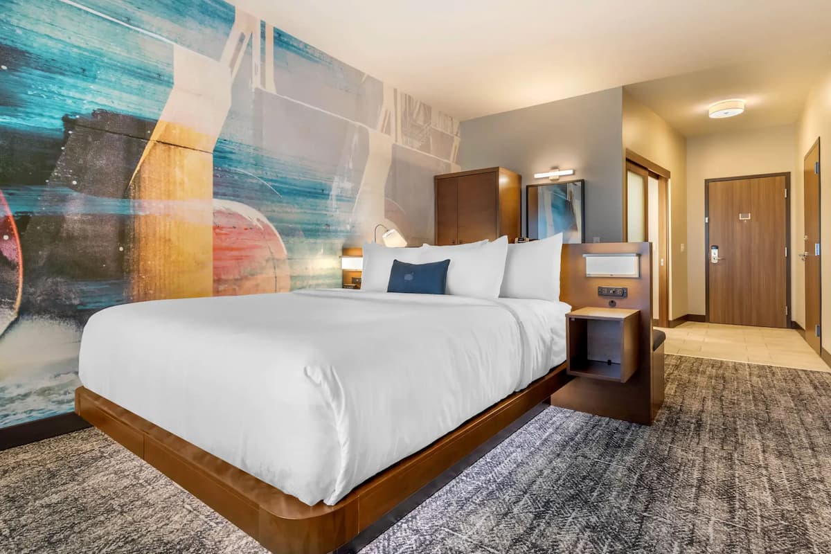 A hotel room with a large bed, a nightstand, a wall-mounted TV, and a door.