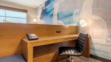 Une chambre d’hôtel avec un bureau en bois, un fauteuil de bureau noir, un téléphone et un mur orné d’œuvres d’art abstraites.