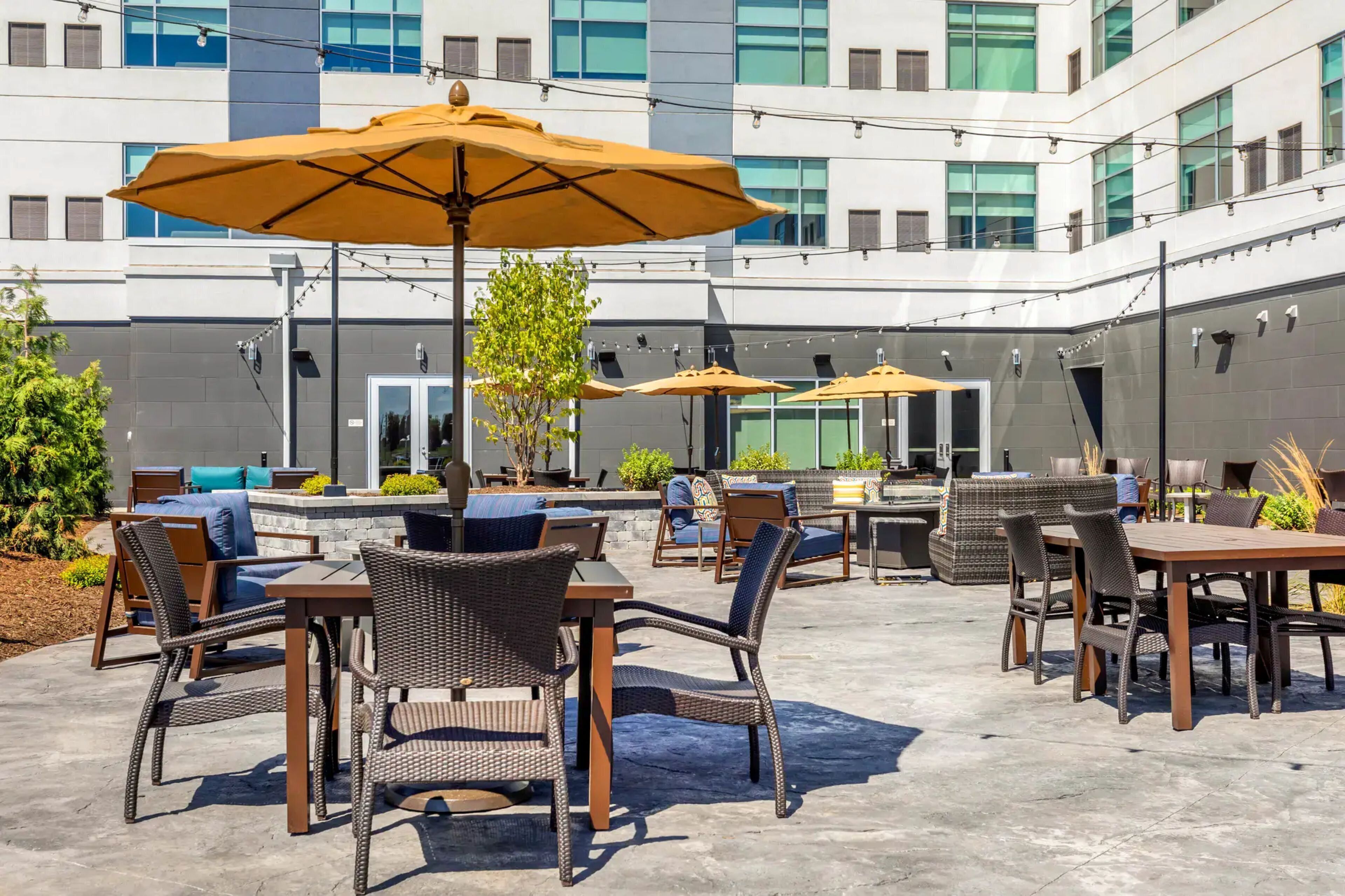 Un espace extérieur aménagé en terrasse, avec des meubles en osier, des parasols jaunes et un bâtiment moderne en arrière-plan.