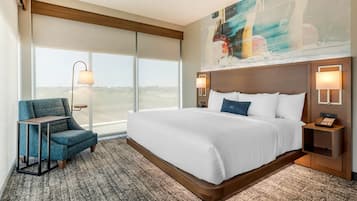 A hotel room with a large bed, a chair, a desk, and a painting on the wall.