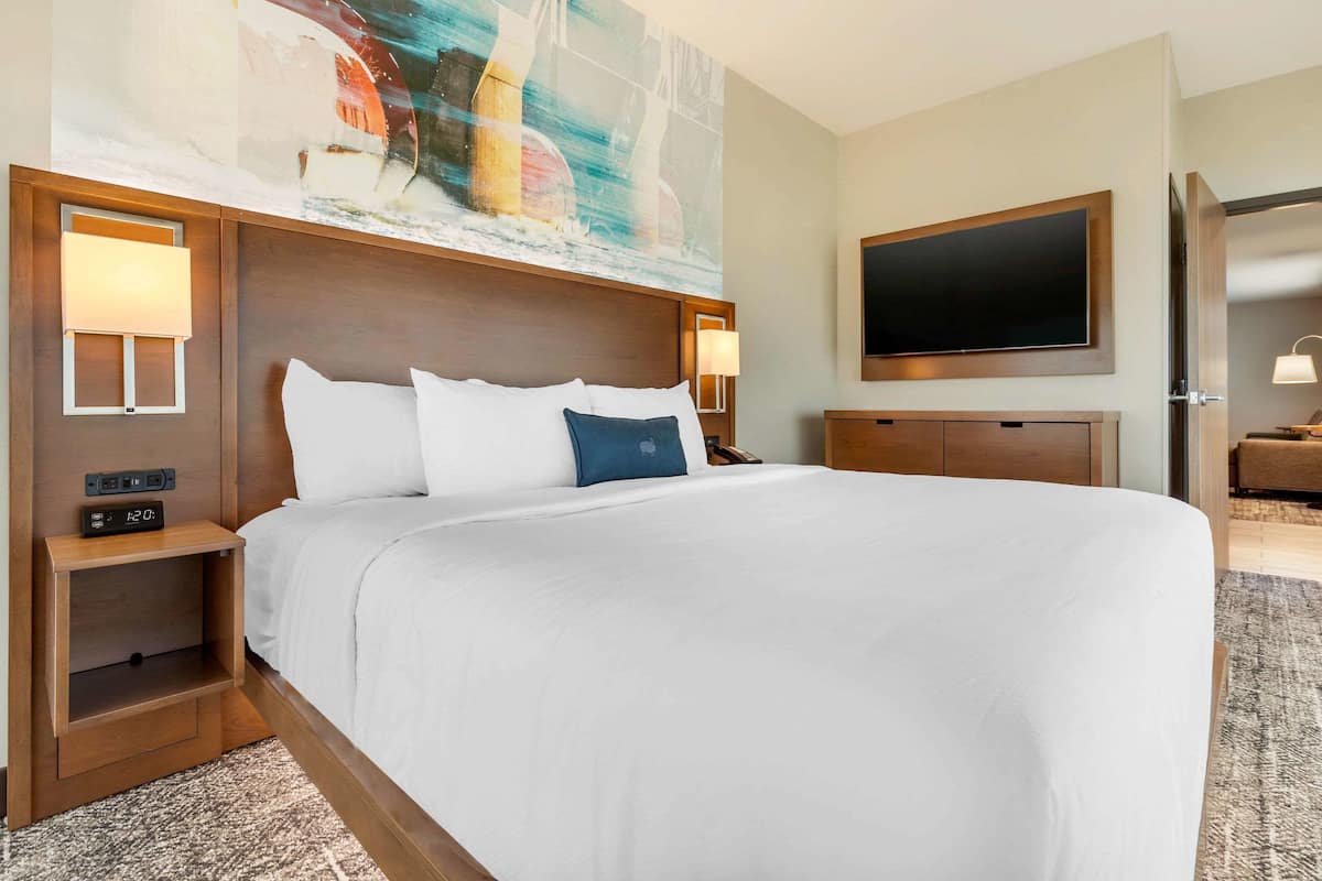 A hotel room with a large bed, a flat-screen TV, a nightstand, and a painting on the wall.