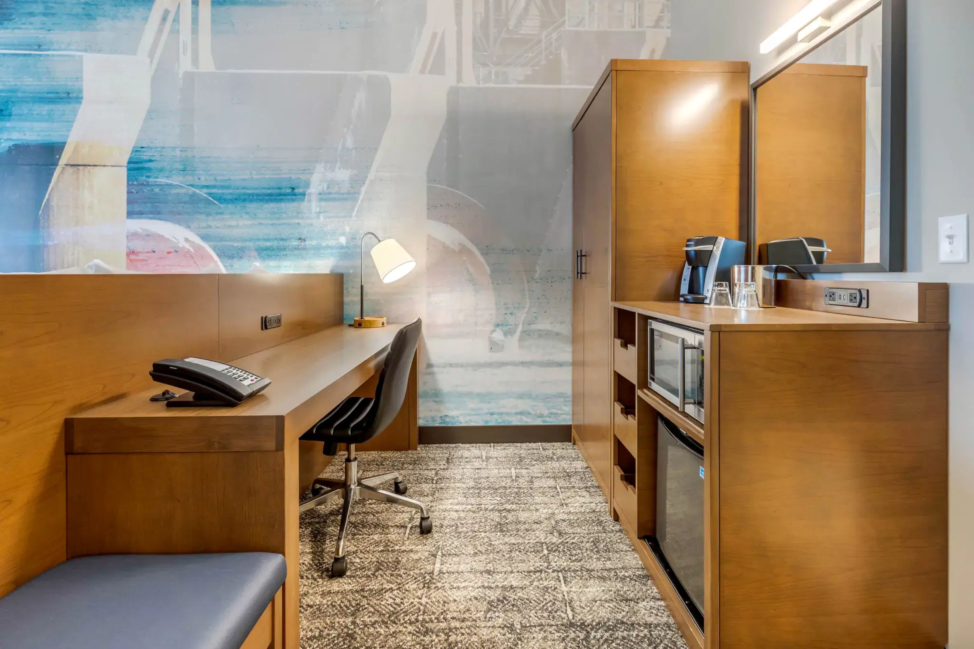 A hotel room with a desk, chair, and a large mirror.