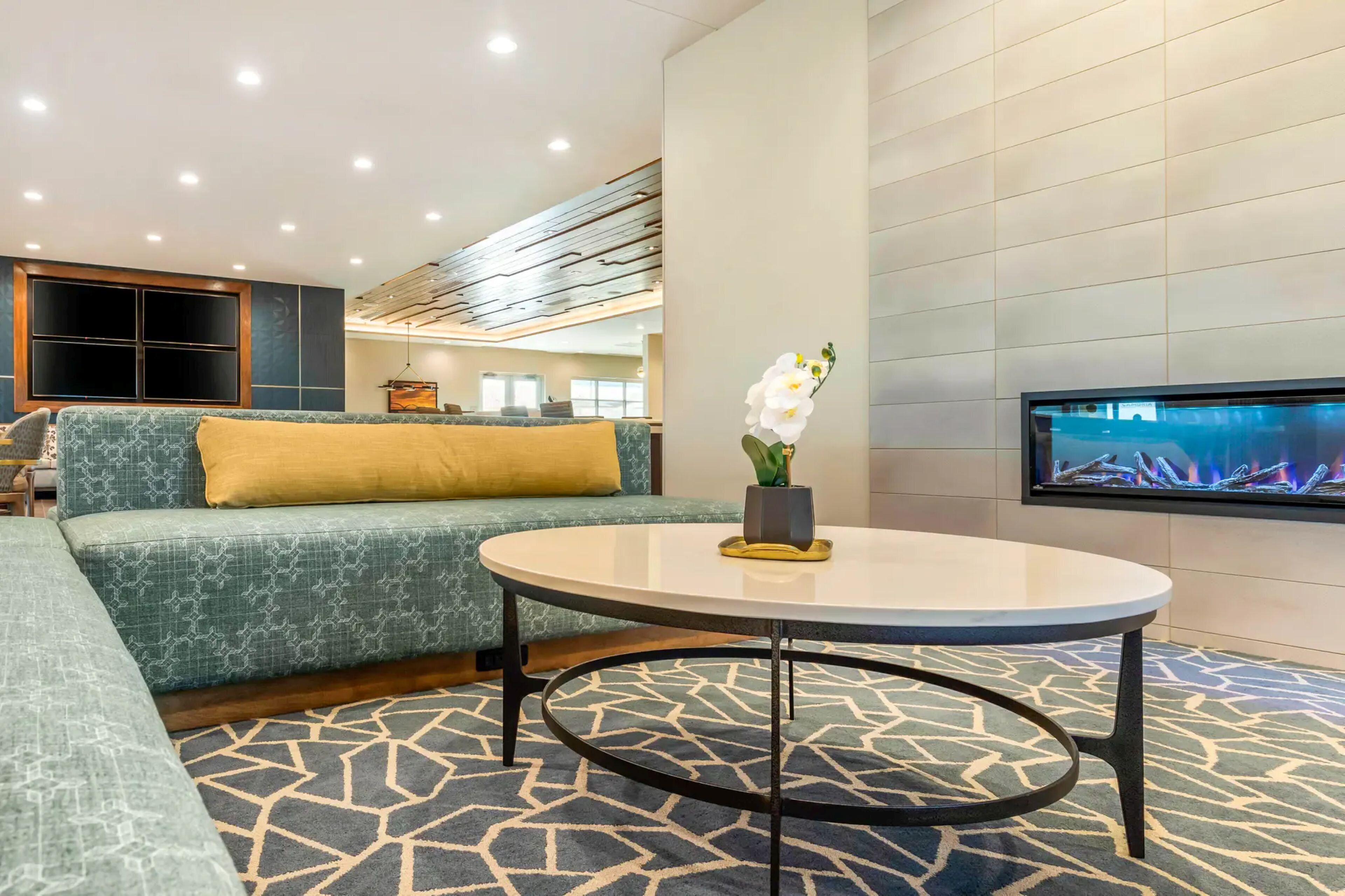 A modern living room with a green sofa, a round coffee table, and a flat-screen TV mounted on the wall.