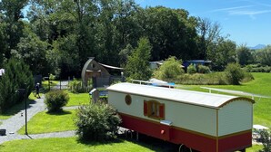 A mobile home with a red and white exterior, situated in a lush green park with trees and a clear sky. - Belle Epoque Trailer of Saint-Pardoux 63440 2 places (Saint-Pardoux)