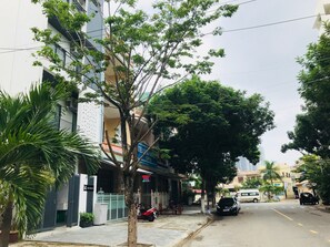 A street view with a building featuring a gated entrance, a tree in the foreground, and parked vehicles. - Affordable and Quiet Studio near Dragon Bridge (Da Nang)