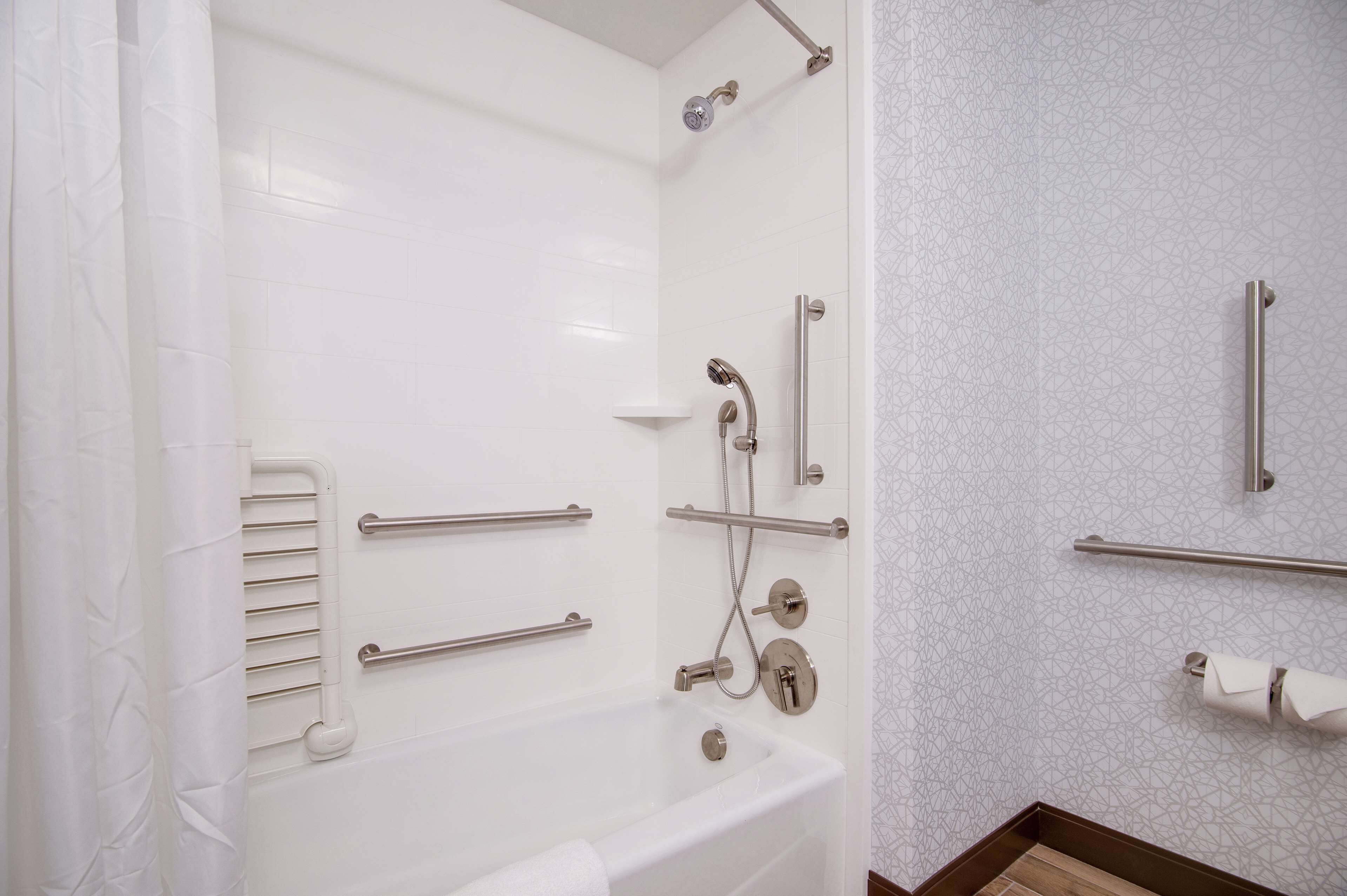 A modern bathroom with a bathtub, grab bars, a showerhead, and a toilet paper holder.