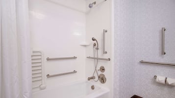 A modern bathroom with a bathtub, grab bars, a showerhead, and a toilet paper holder.