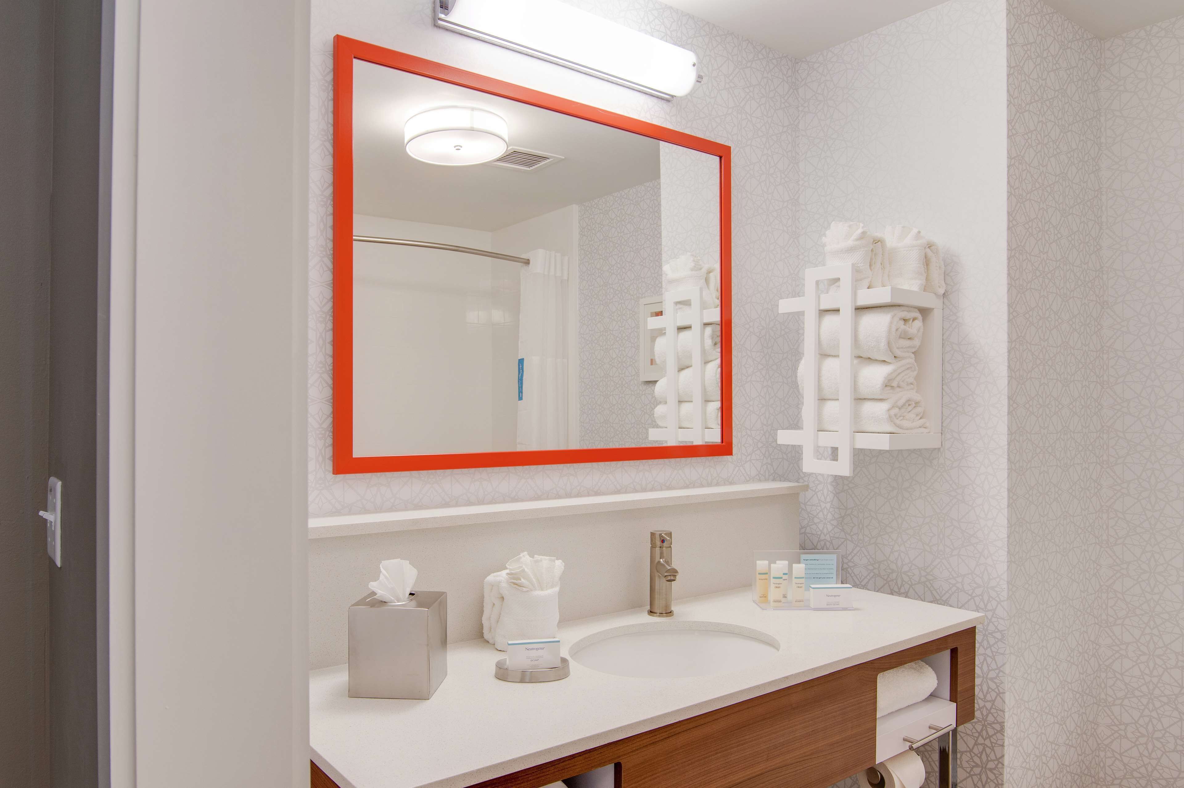 A bathroom with a large mirror, a sink, and a towel rack.