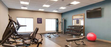 A gym with cardio machines, dumbbells, and a red exercise ball.