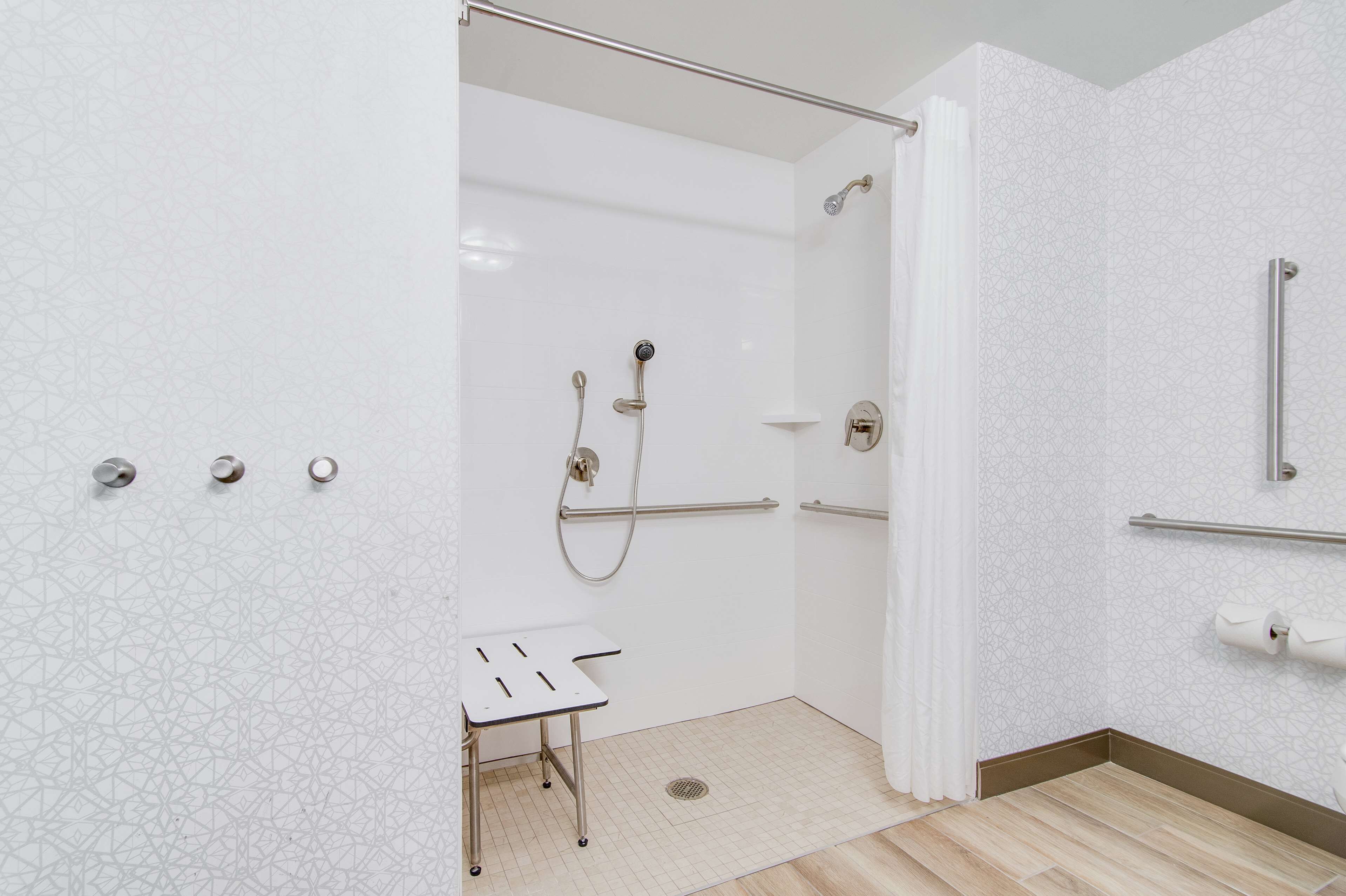 A modern bathroom with a shower, grab bars, a small table, and a toilet with a handrail.