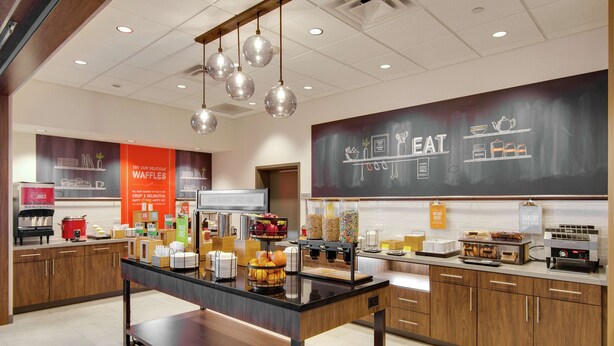 A modern kitchen area with a central island, various food items, and a chalkboard menu.