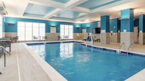 An indoor swimming pool with clear blue water, surrounded by lounge chairs and tables, and a ceiling with a geometric design.