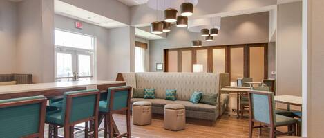 Un moderno vestíbulo de hotel con zona de bar, arreglos de asientos y mostrador de recepción.