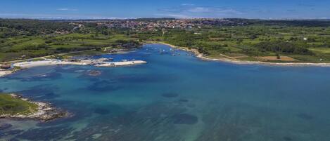 An aerial view of a coastal area with clear blue waters, a marina with boats, and a distant town.