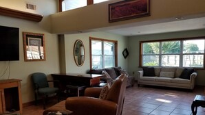 A spacious living room with a large window, a fireplace, and a television mounted on the wall.