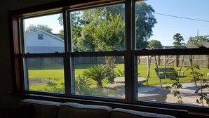 A room with a large window overlooking a backyard with a lawn, a wooden deck, and a house in the background.