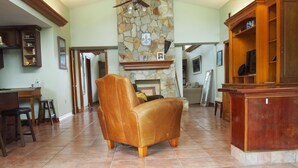 A spacious living room with a stone fireplace, a leather armchair, a wooden coffee table, and a television on a wooden stand.