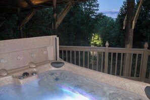 Ein Whirlpool mit Holzterrasse und Geländer, umgeben von Bäumen.