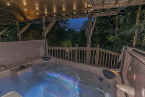Een hottub met een houten terras en uitzicht op bomen in de schemering.