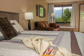 Une chambre d’hôtel avec un grand lit, un canapé, une fenêtre donnant sur des arbres et des montagnes, et une porte.