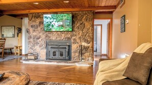 A cozy living room with a stone fireplace, wooden ceiling, and a television mounted on the wall. - Enjoy Starry Nights, Views, Privacy & Woods- Hot Tub, Game Room, Dog-Friendly (Gatlinburg)