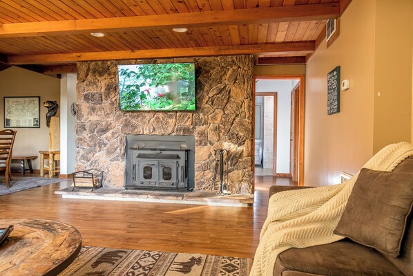A cozy living room with a stone fireplace, wooden ceiling, and a television mounted on the wall. - Enjoy Starry Nights, Views, Privacy & Woods- Hot Tub, Game Room, Dog-Friendly (Gatlinburg)