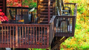 A wooden deck with chairs and tables, surrounded by autumn foliage. - Enjoy Starry Nights, Views, Privacy & Woods- Hot Tub, Game Room, Dog-Friendly (Gatlinburg)