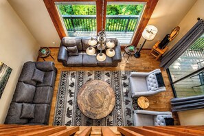 Ein Wohnzimmer mit hohen Decken, einer Couch, Sesseln, einem Couchtisch und einer Pendelleuchte.