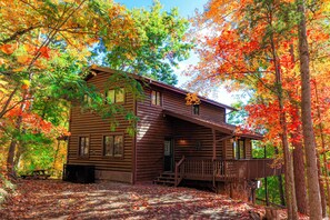 A log cabin with a porch, surrounded by autumn foliage.