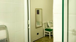 A narrow hallway with white tiled walls and a door leading to a room with a green chair and a framed picture on the wall. - Charming studio 5 mins walk from Copacabana beach (Copacabana)